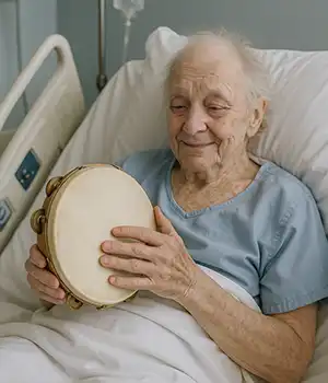 an elderly man in a hospital bed smiles softly while playing the tambourine